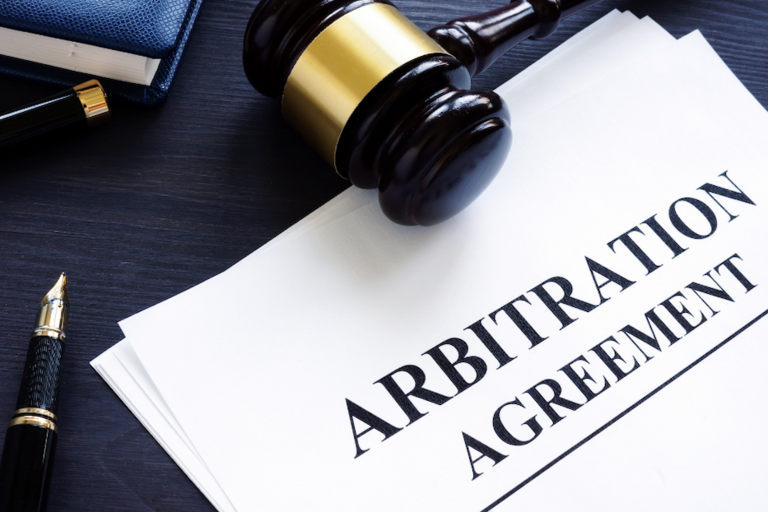 Image of document titled "arbitration agreement", a gavel, and a pen lying on a table top.