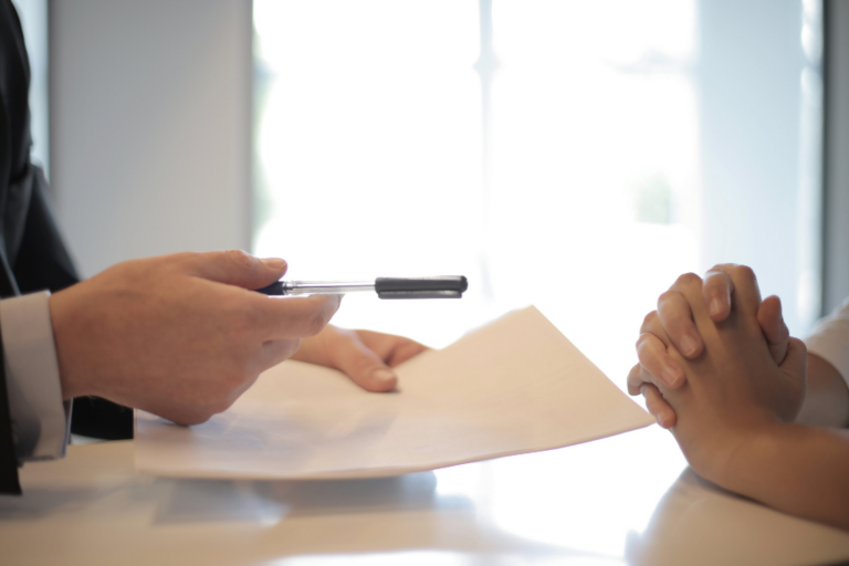 Image of person handing over a contract and pen to another individual.