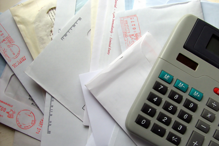 Image of a pile of bills received in the mail and a calculator.