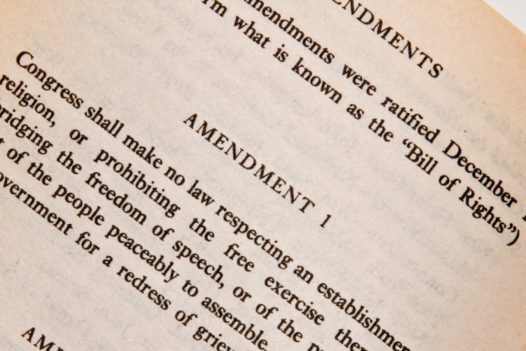 Diagonal image of black printed text of the first amendment of the US Constitution, on light brown paper.