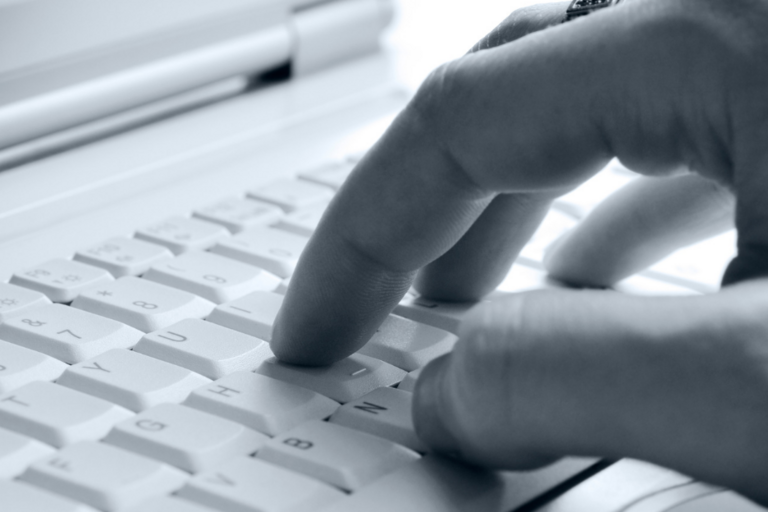 Close up image of hand typing on laptop keyboard, in black and white.