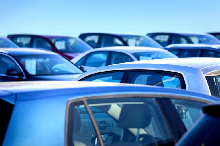 Image of the roofs of several cars in a lot for sale, with a clear blue sky above.