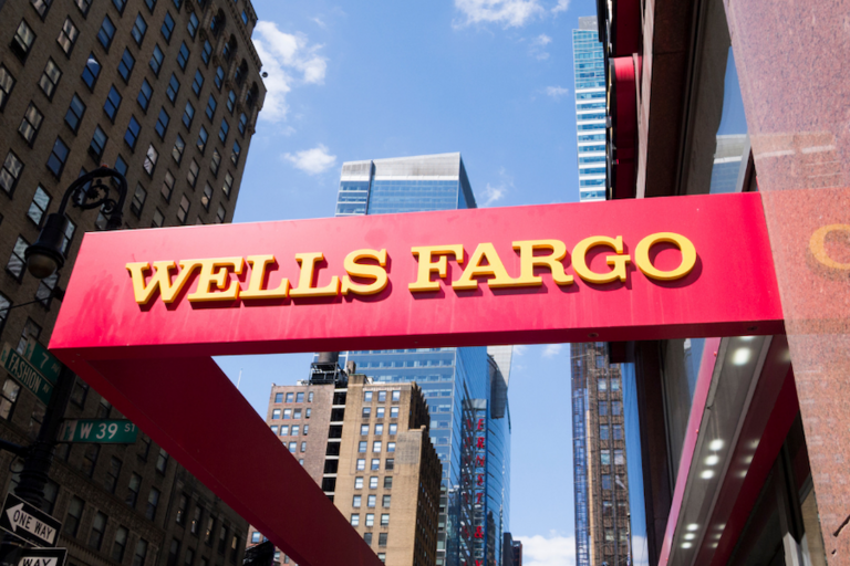 Red Wells Fargo sign against urban backdrop and blue sky.