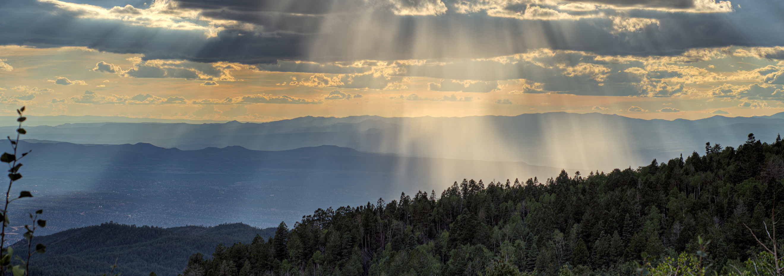 Image of Santa Fe valley in New Mexico, with rays of sunlight beaming through scattered clouds above.